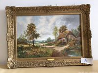 Front view of framed picture showing detailed countryside print and ornate gold frame