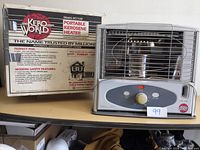 Front view of Kero World Portable Kerosene Heater model KC1100 alongside retail box showing product details and safety information. Heater features metal grill and control panel with knob and buttons.