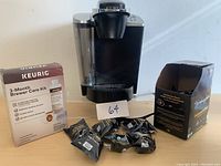 Keurig coffee maker with attached water reservoir, 3-Month Brewer Care Kit, box of coffee pods, and loose coffee pods in front.