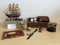 View showing whole collection including ship model, wooden desk organizer, brass moose bookend, watches, carved wooden plaque, small clock, miniature car, pocket watch, and small brass figurines.