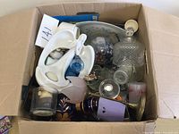 Top view of box showing varied knick knacks including white ceramic figurine, cut-glass container with lid, blue glass items, and other decorative pieces