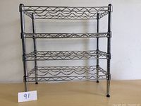 Front view of the four-tier metal wine rack showing wire grid shelves and support legs.