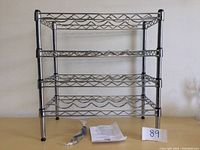 Full assembled metal wine rack with four horizontal tiers to hold wine bottles, placed against a light wall.