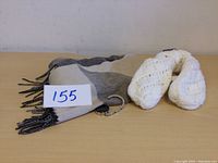 Scarf folded with tag visible, and white knitted mitts placed beside it on light wood surface.