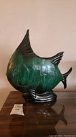 Front view of the green and black ceramic fish-shaped vase on a wooden surface.