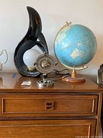 Photo showing the three items: a black ceramic lamp, metal clock, and world globe displayed together on wooden furniture.