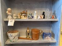 Shelf with assorted porcelain and glass figurines including angels, cats, swans, birds, and children, along with a wooden flute and ceramic flower pots.