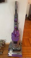 Full view of the Dyson upright vacuum cleaner showing purple and gray color scheme and dust container.