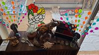 Wide view of various figurines and decorative items arranged on a wooden surface including glass peacocks, a stained glass bird, wooden animal figurines, metal spoons, a seashell, and a box with small collectibles.