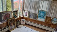 Overall view of nine framed art prints placed on floor and leaning against walls and window with varying subjects and frame styles