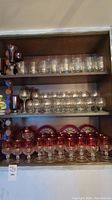 Shelf arrangement of clear Olympic glasses with gold logos on top and middle shelves, red glasses and red plates below