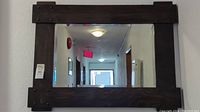 Full view of the mirror showing the dark wood frame and reflection of hallway ceiling lights and exit sign.