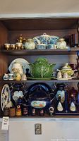 Two-shelf overview showing top row brass-tone coffee pot with goblets and blue/floral porcelain tea set