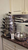 Stacked set of stainless steel pots with lids on a granite countertop next to a frying pan, showing overall lot contents.