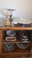 Overview of crystal and silver-plated serving dishes on wooden shelving unit