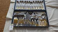 Full view of the cutlery set showing all items in the case including knives, forks, spoons, butter knives, and serving utensils with gold details.