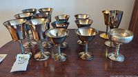 Front view of a group of 14 silver plated wine goblets set on a wooden table, showing their twisted stems and tarnishing.