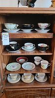 Shelf displaying eleven assorted teacups and saucers in various floral and color patterns