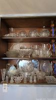 Shelf displaying assorted vintage cut glassware and metal tray arranged neatly, showing size and variety of items.