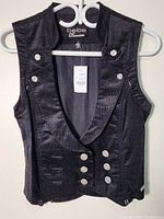 Front view of the black velvet woman's vest hanging on a white hanger, showing the double row silver buttons and sleeveless design.