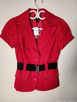 Front view of red women's blazer showing puffed sleeves, button closure, two front pockets, and black elastic belt.