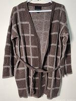 Full view of the Cynthia Rowley brown and beige checkered long sweater with belt hung on a hanger, front facing.