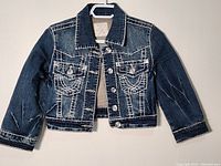 Full view of new L.A.IDOL USA women's denim jacket in size small, showing front cut, collar, and sleeve details on blue denim fabric with white stitching and buttons.