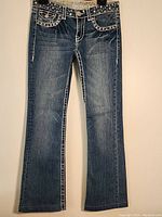 Front view of dark blue denim stretch pants with decorative white stitching and embellished front pockets.