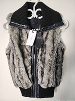 Front view of a woman's silver grey faux fur vest with thick ribbed black knit collar hanging on a white hanger.