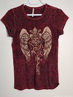 Full front view of the burgundy women's top showing wing and fleur-de-lis design with jewel accents.