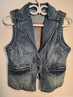 Front view of the women's denim vest on a hanger showing collar, front button closure, and pockets.