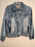 Front view of light blue denim jacket showing zipper closure and pockets.