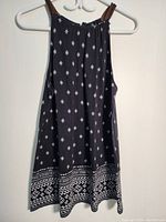 Full view of black sleeveless top with shoulder straps hanging on a white hanger on a wall.