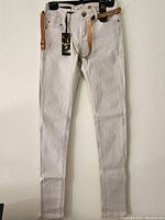 Front view of ivory super skinny stretch pants hanging with attached belt and original tag visible.
