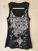 Front view of the black sleeveless women's top with ornate silver and white fleur-de-lis graphic print.