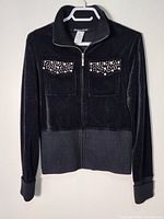 Front view of black velvet blazer showing full zipper closure, high collar, ribbed knit cuffs and bottom hem, decorative silver-tone studded chest pockets.