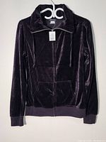 Front view of black velvet women's blazer by Seductions hung on a white hanger against a pale wall, showing full front zip and hood.