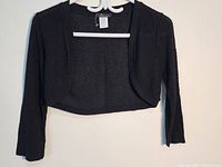 Black knitted women's cover top hanging, showing front and overall design.