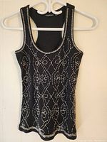 Front view of black sleeveless tank top with bead decorations hanging on white hanger.