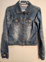 Full front view of the blue denim jacket showing the collar, chest pockets with button flaps, and button closure.