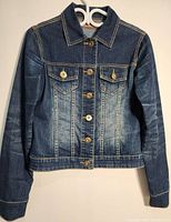 Front view of the navy blue denim jacket hanging on a hanger showing button-up front, collar, long sleeves, and two chest pockets with button flaps.