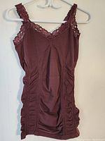 Front view of sleeveless dressy top hanging on a white hanger against a light wall, showing lace neckline and front ruching detail.