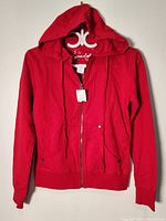Front view of a red women's hoodie by Seductions with hood, zipper, and front pockets with snap buttons.