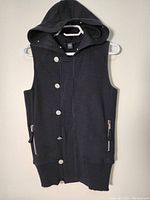 Front view of black sleeveless hoodie with hood on hanger