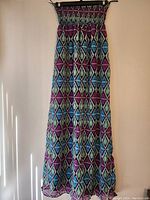 Full view of the strapless long dress with multicolored geometric diamond and triangle patterns hung against wall.