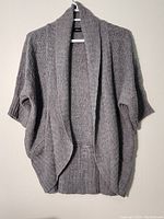 Front view of silver grey wool sweater hanging on a hanger showing overall shape and textured knit pattern.