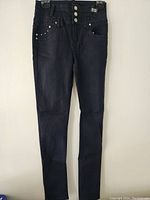 Front view of black skinny fit denim pants showing triple button closure, pockets with metal studs, and overall fitted silhouette.