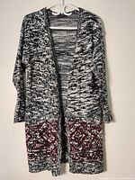 Full view of the black, white, and gray marled knit long sweater with open front hanging on a hanger.