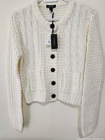 Front view of woman's ivory sweater with black buttons, tags attached showing new condition