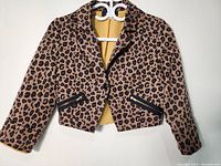 Full view of the leopard print blazer on hanger showing cropped length, button closure, and zippered pockets.